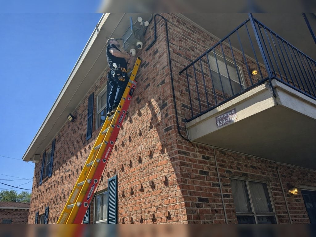 Professional security camera installation on apartment building by Soltek LA in South Louisiana using ladder and exterior surveillance equipment.